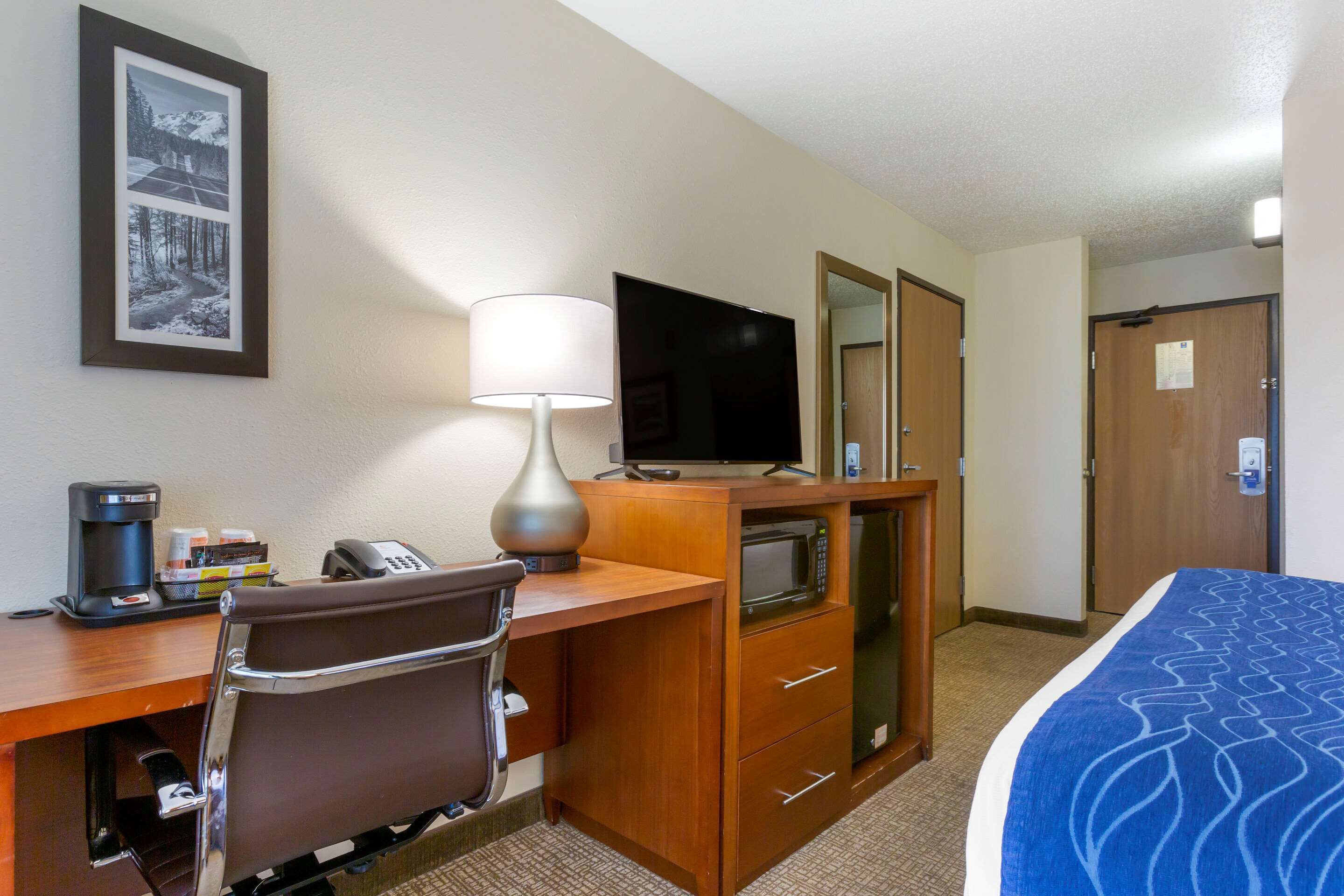 A hotel room with a desk, chair, bed, TV, and a mirror.