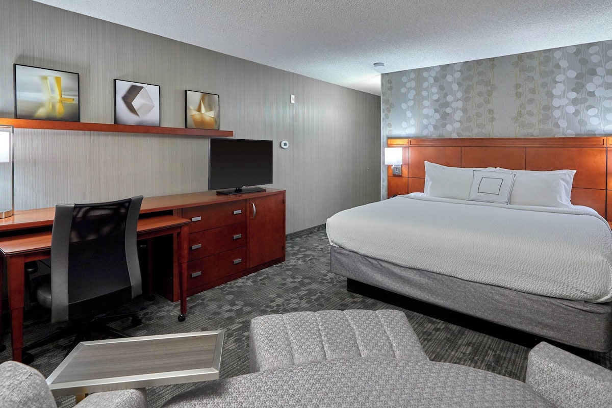 Una habitación de hotel con una cama, un escritorio con una silla, un televisor y un pequeño sofá.