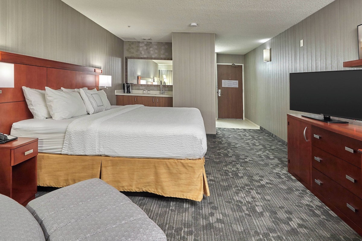 Habitación de hotel con una cama grande, televisión, escritorio y baño visible a través de una puerta abierta.