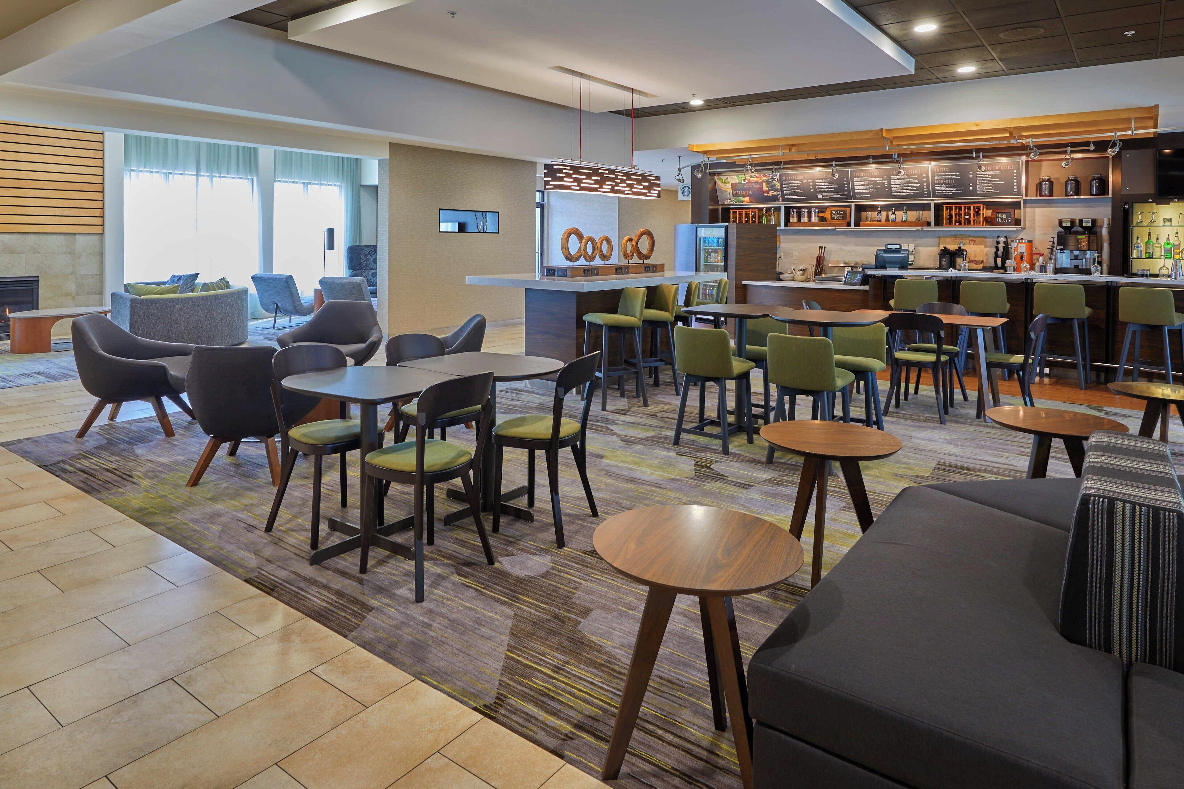 A modern hotel lobby with a bar area, seating arrangements, and a fireplace.