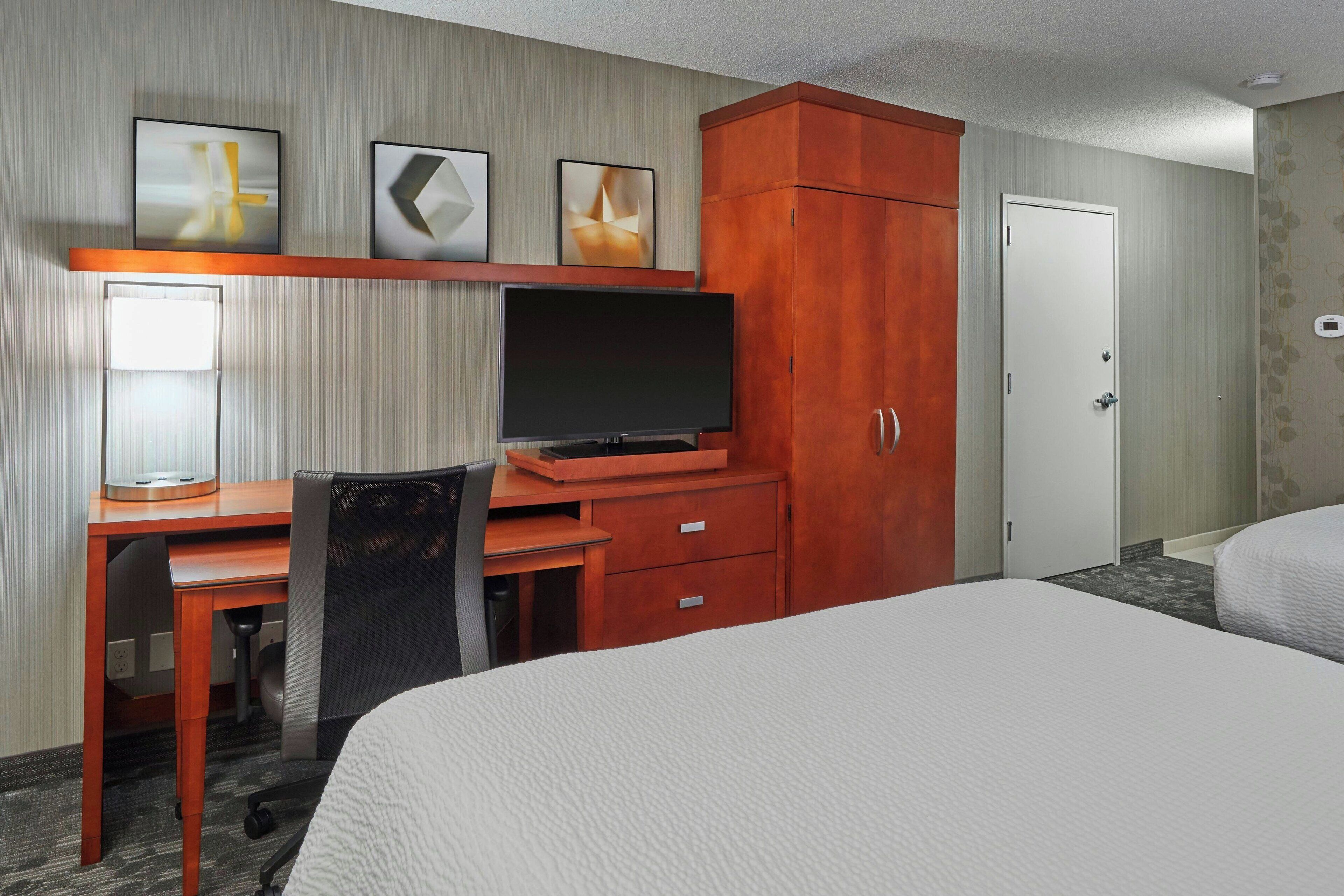 A hotel room with a bed, a desk with a computer, a television, and a wardrobe.