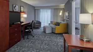 Een hotelkamer met een bureau, stoel, bank, poef en een televisie.