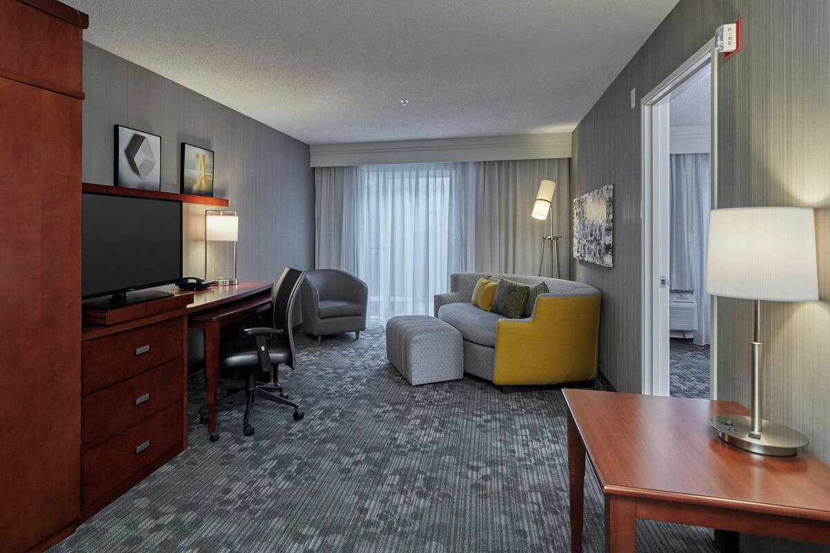 Habitación de hotel con escritorio, silla, sofá, otoman y televisor.