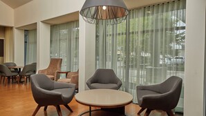 Een moderne zithoek met een ronde tafel en drie stoelen, grote ramen met dunne gordijnen en een hanglamp.