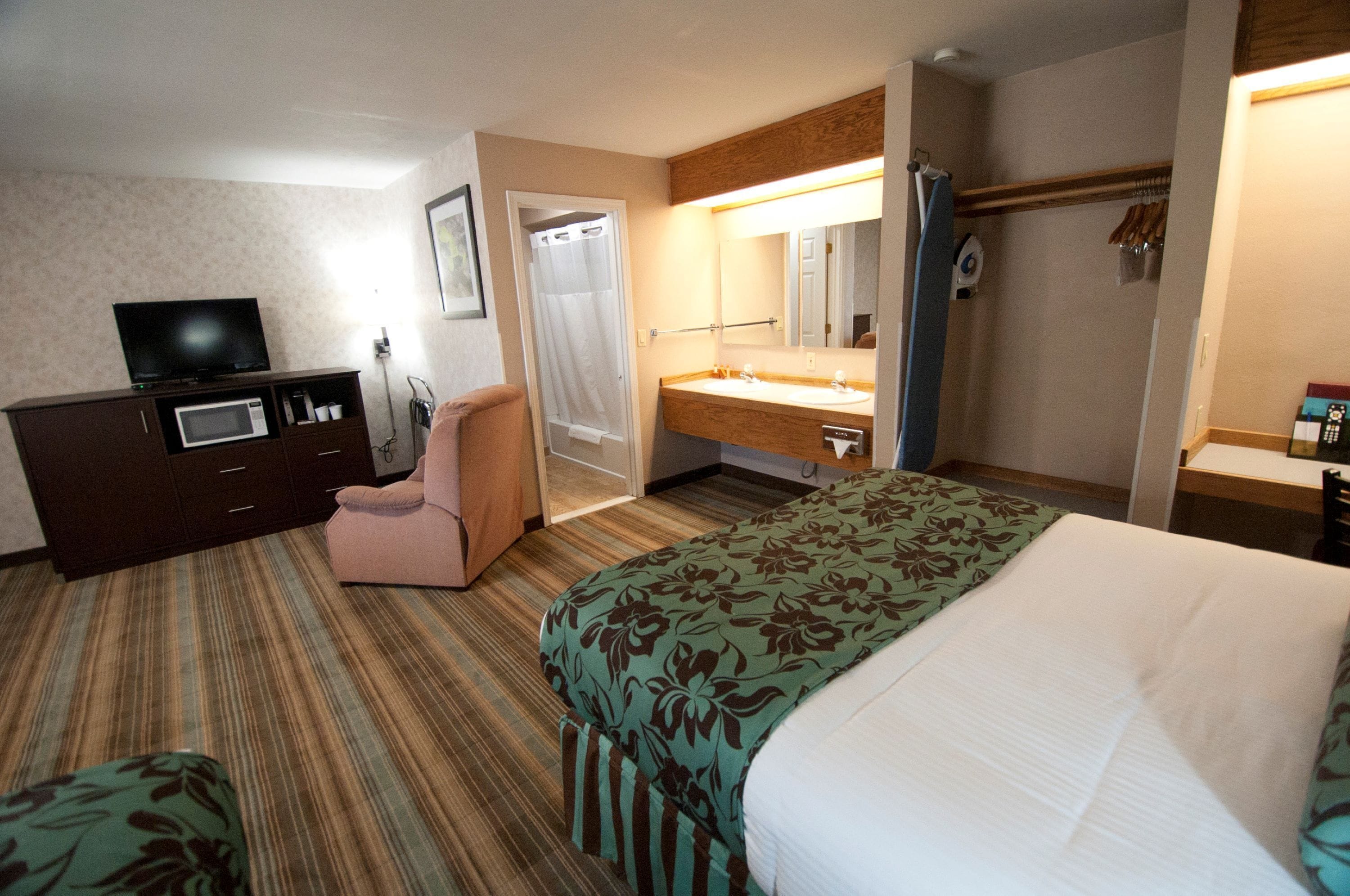 A hotel room with a bed, a desk with a computer, a TV, a bathroom with a shower, and a sink.