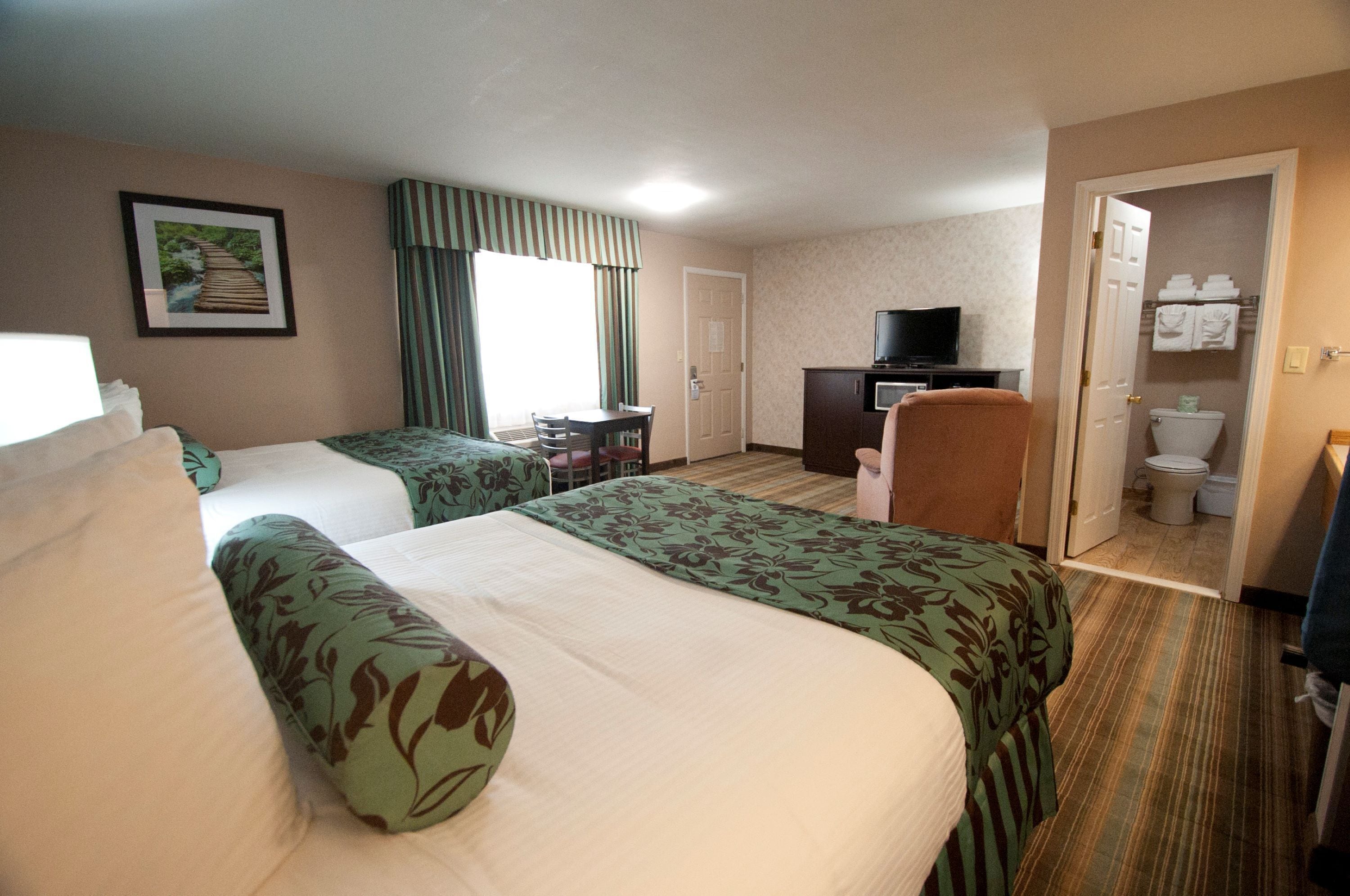 A hotel room with two beds, a desk, a television, and a bathroom visible through an open door.