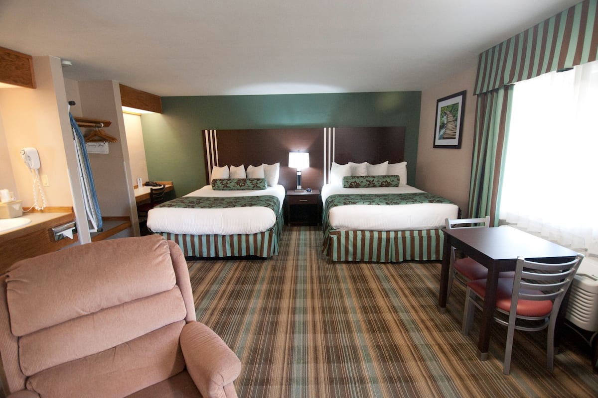 Habitación de hotel con dos camas, un escritorio, una silla y una ventana con cortinas.