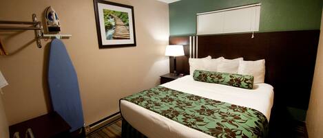 Habitación de hotel con cama bien hecha, mesita de noche con lámpara, un cuadro en la pared y ventana con persianas.
