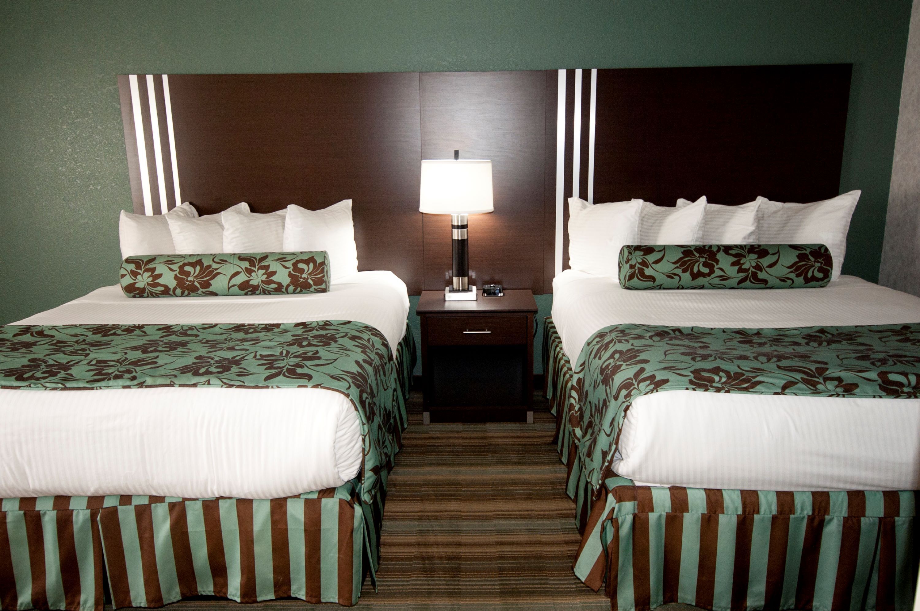 A hotel room with two beds, a nightstand, and a lamp.