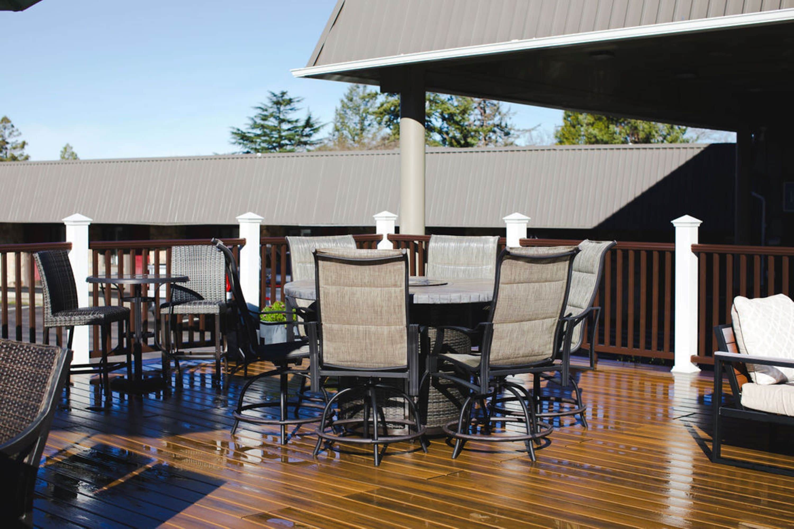 Una terraza de madera con mobiliario exterior, que incluye sillas y una mesa, bajo una zona cubierta con techo metálico.