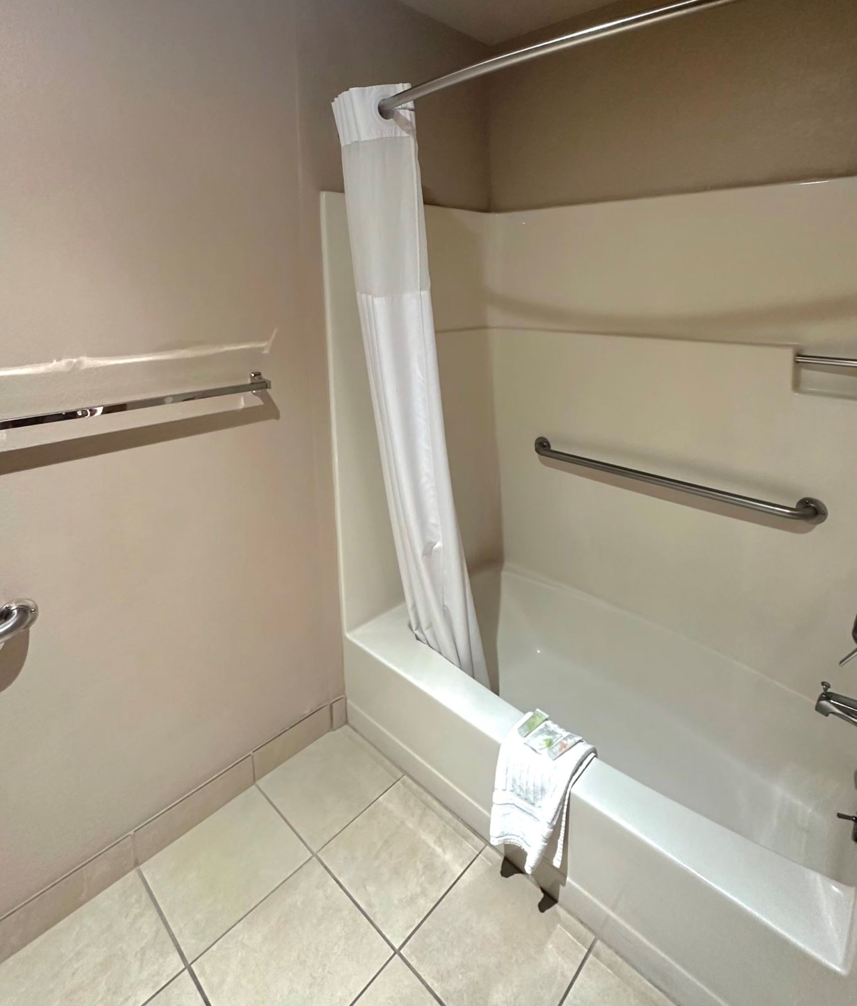 A bathroom with a bathtub, a shower curtain, a towel rack, and a handrail.