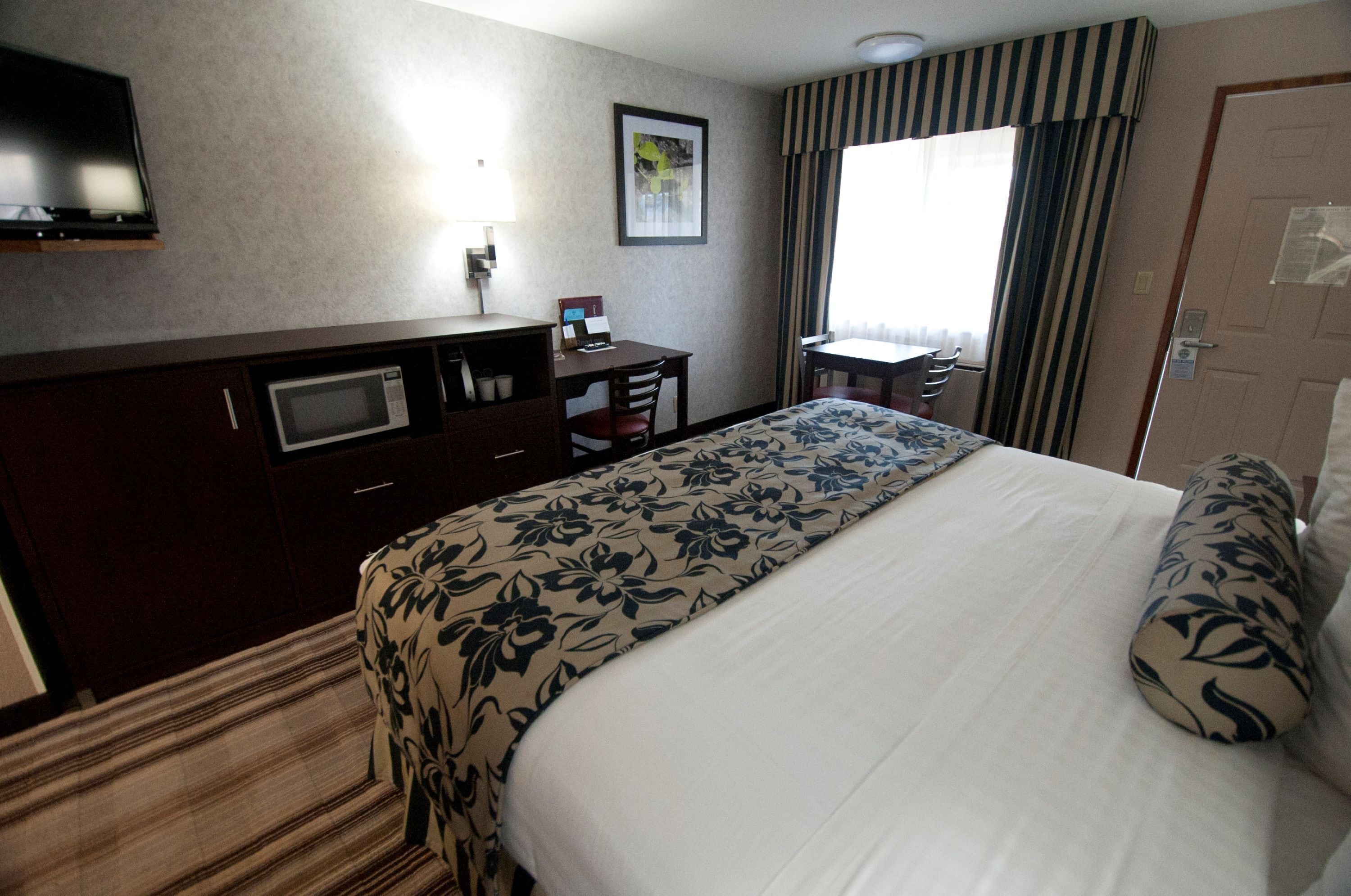A hotel room with a bed, a desk, a chair, a television, and a window with curtains.