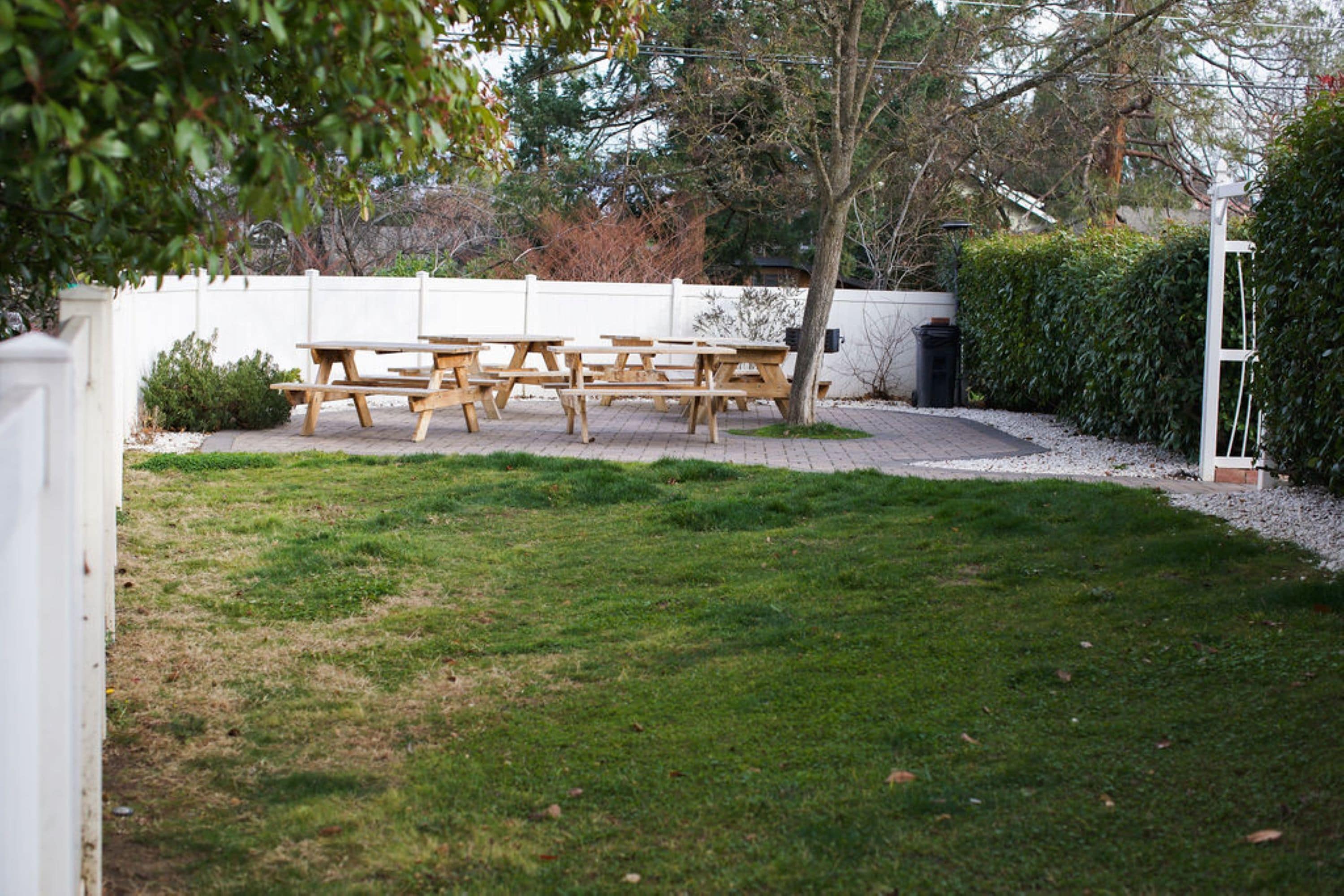 A grassy outdoor area with picnic tables and a white fence.