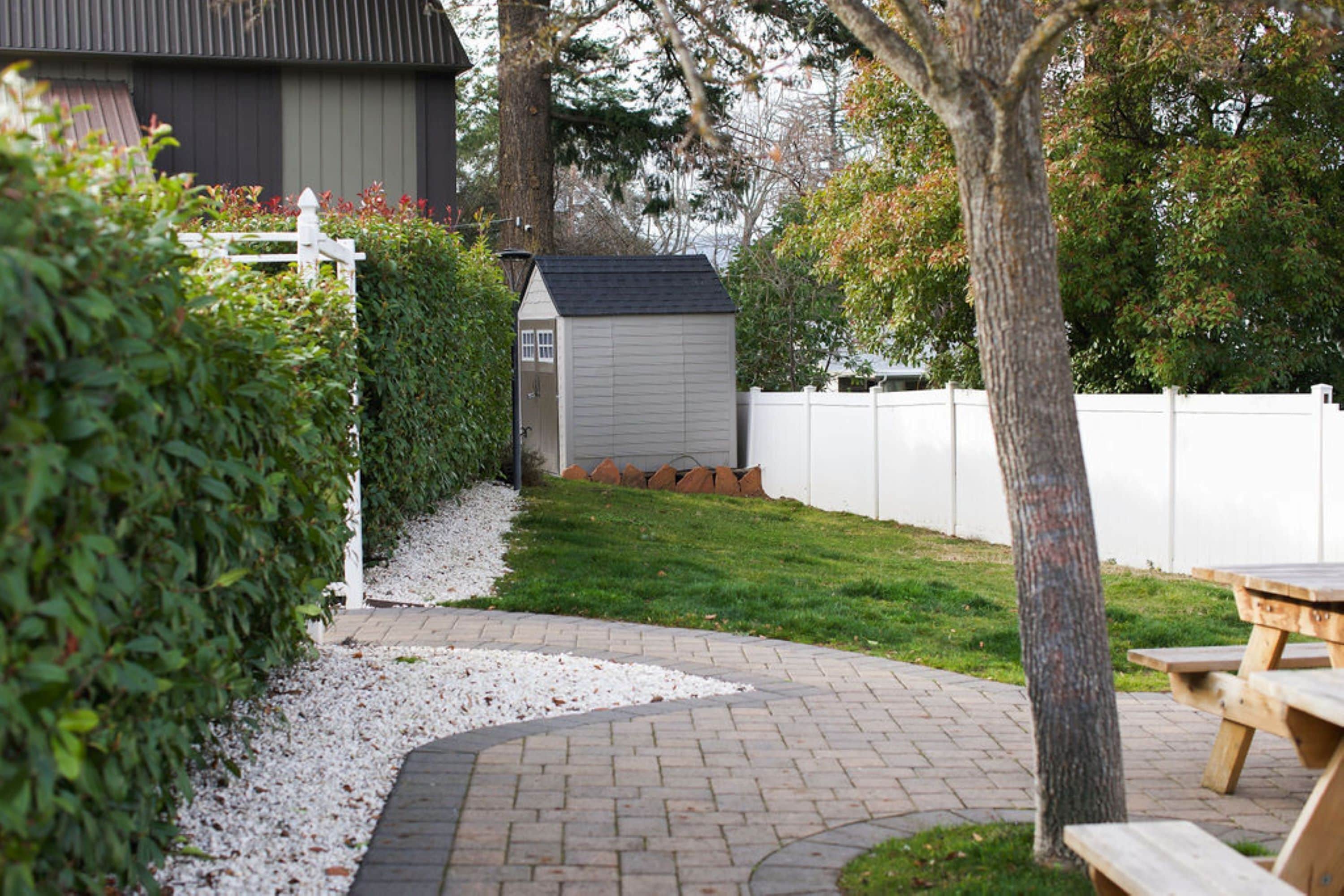 A backyard with a wooden deck, a shed, and a white fence.