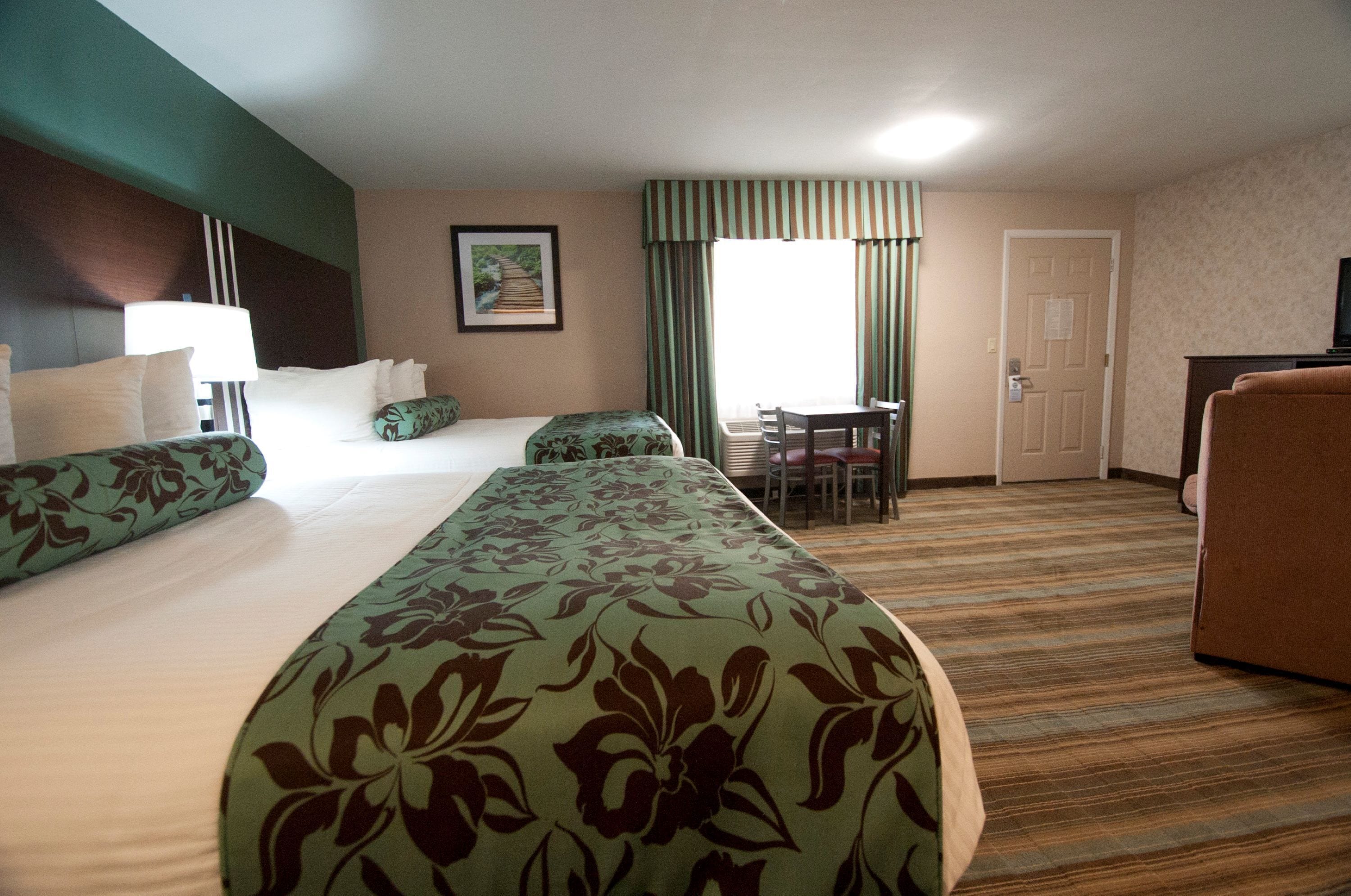 A hotel room with a large bed, two smaller beds, a desk, and a television.