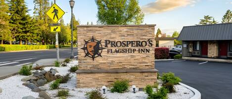 Un letrero para Prosper's Flagship Inn con un logo de estrella y sol, rodeado de un área ajardinada con grava blanca y plantas pequeñas.
