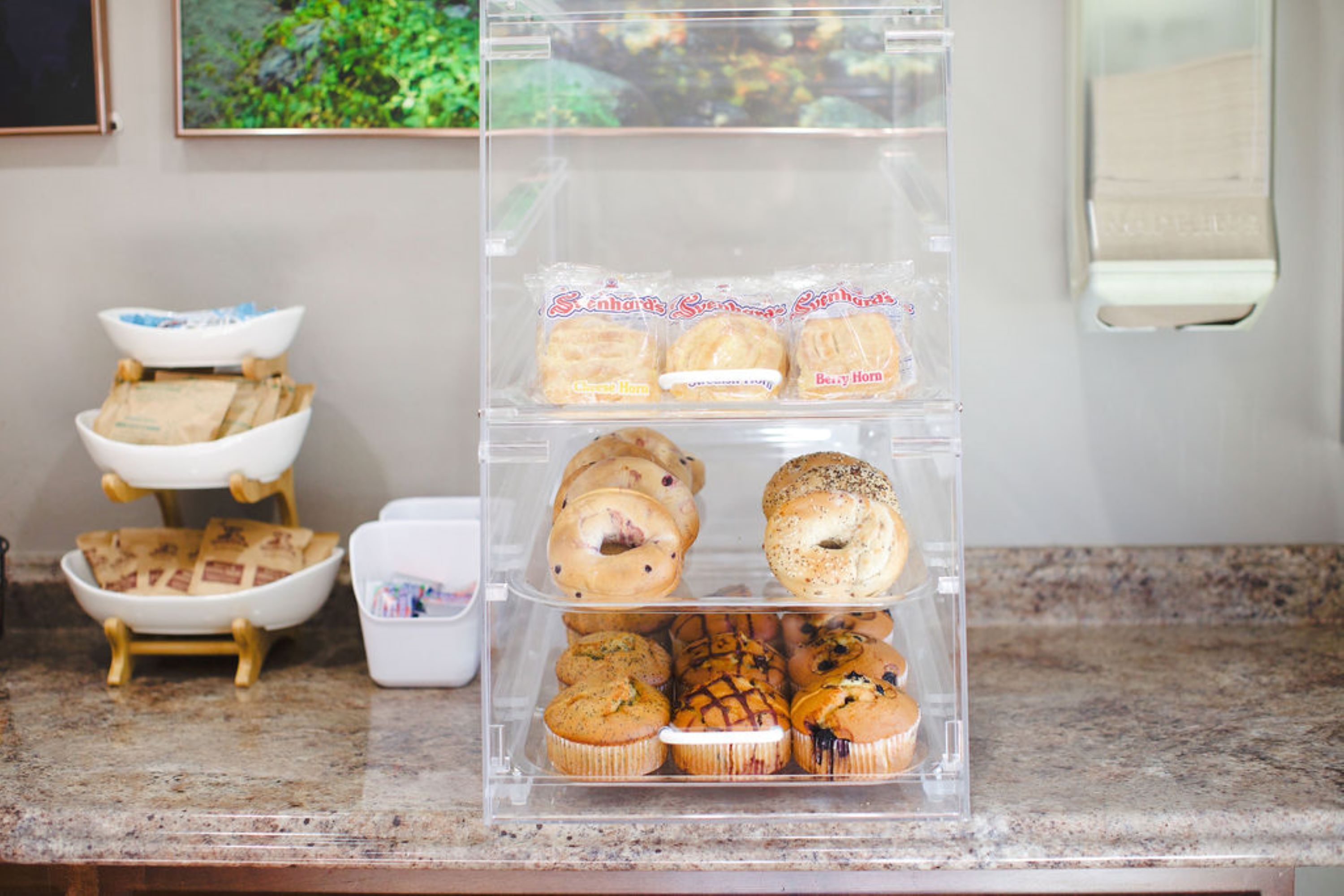 A clear plastic display case with various baked goods on a kitchen counter.