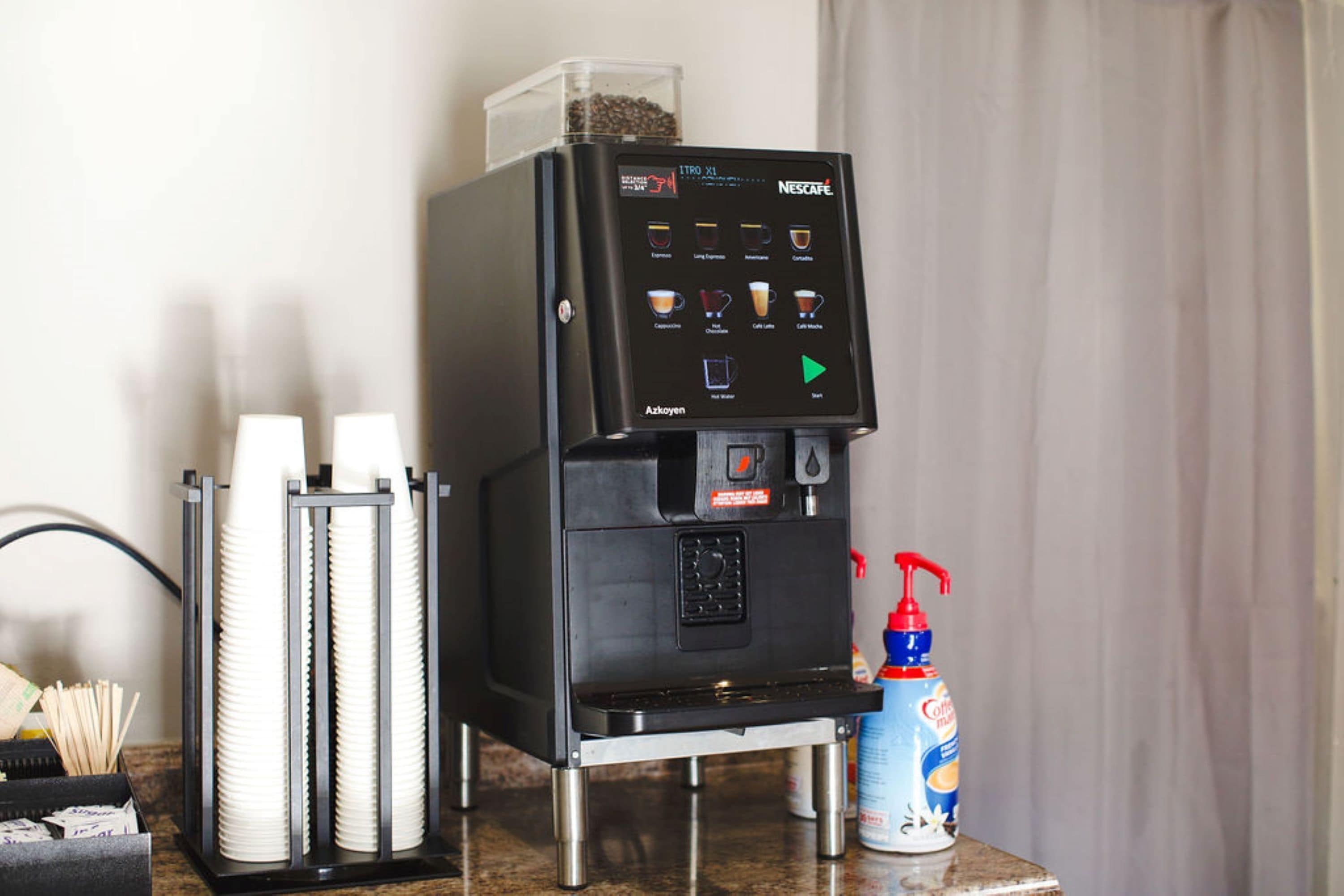 A Nescafe coffee machine with a digital interface, a coffee pod holder, and a bottle of Nescafe instant coffee.