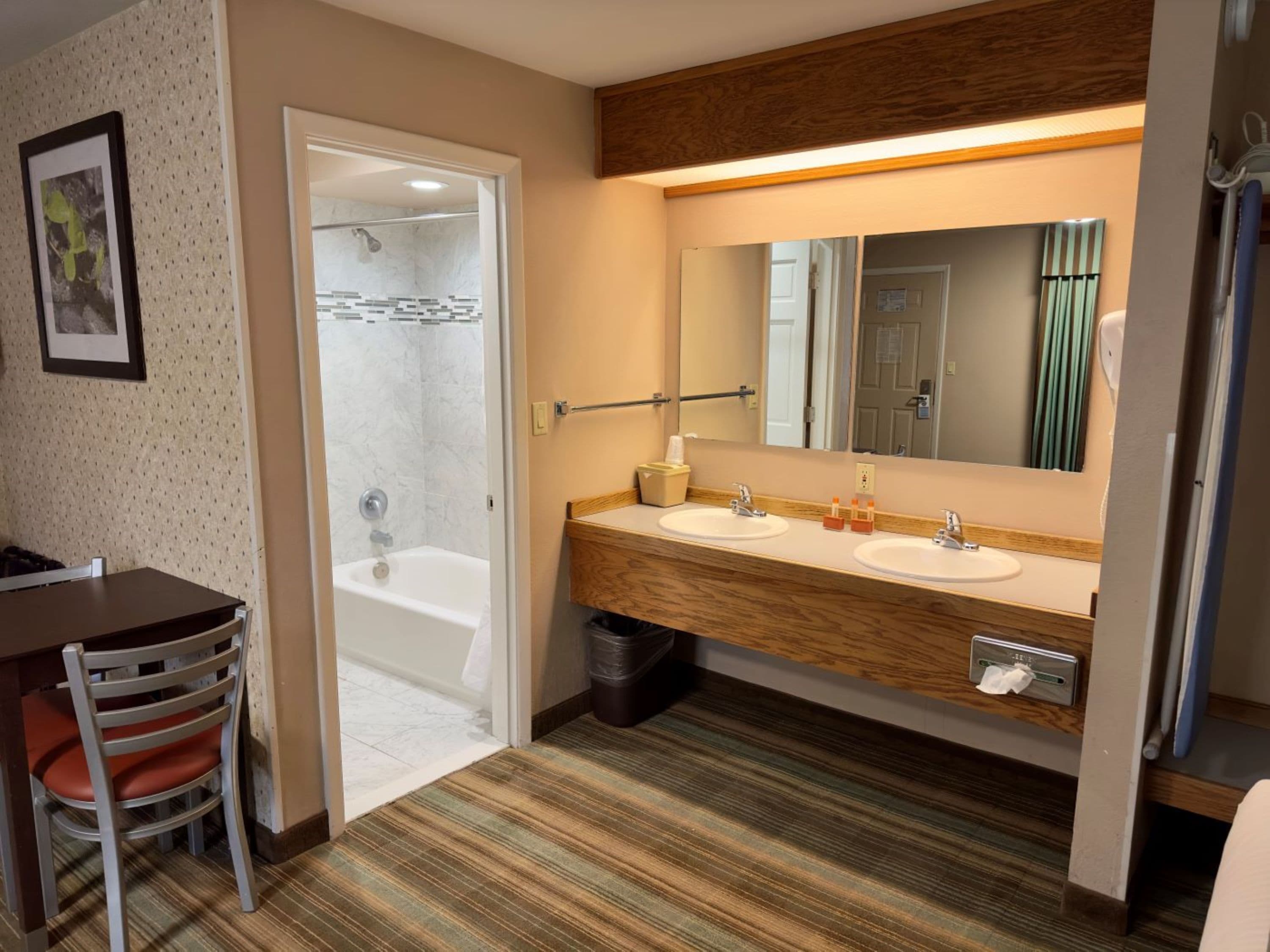 Une salle de bain d’hôtel équipée d’une douche, de deux lavabos, d’un miroir et d’un meuble-lavabo en bois.