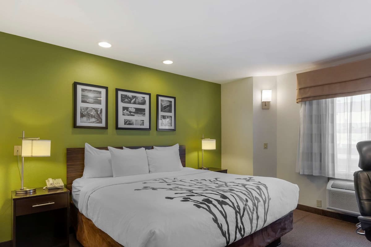 A hotel room with a bed, two bedside tables with lamps, a wall-mounted phone, and framed pictures on the wall.