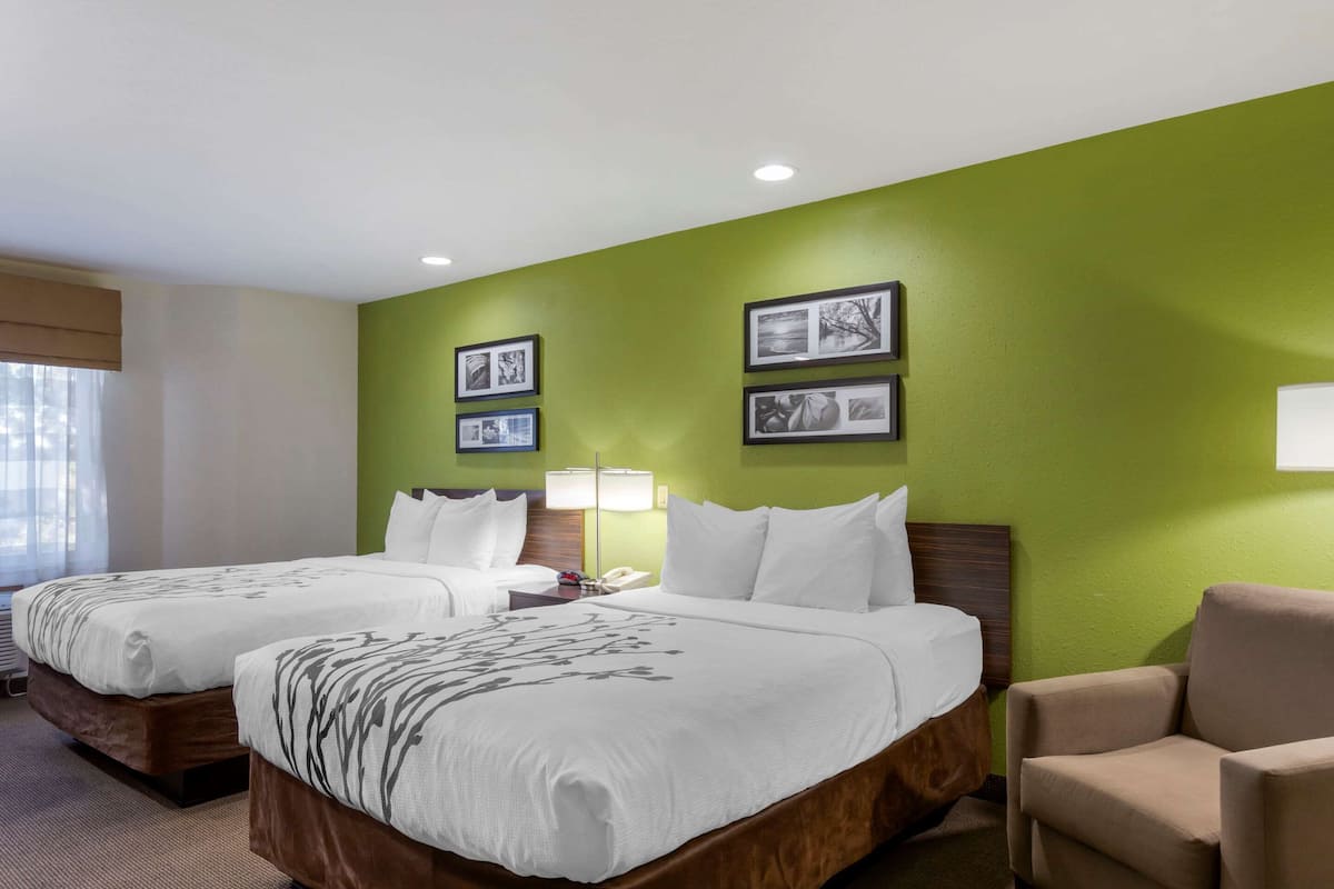 A hotel room with two beds, green walls, framed pictures, a lamp, and a chair.