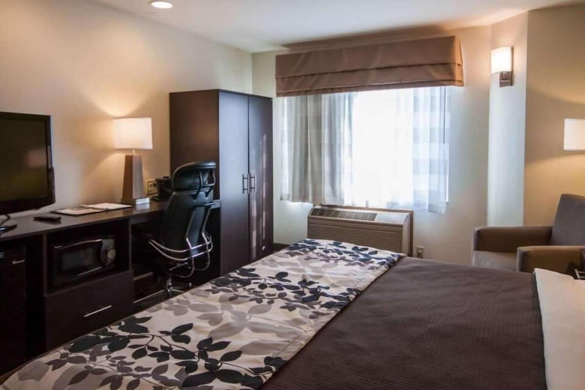 A hotel room with a bed, desk, chair, TV, and window with curtains.