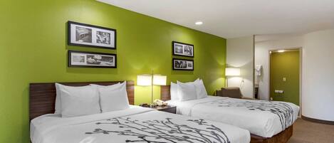 A hotel room with two beds, green walls, framed pictures, and a nightstand with a lamp.