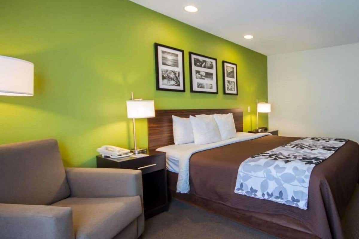A hotel room with a bed, two bedside lamps, a chair, and a nightstand with a phone.