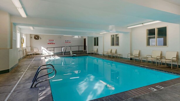 An indoor swimming pool with clear water, a diving board, and several lounge chairs around the pool area.
