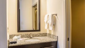 Un baño con lavamanos de encimera de granito, un espejo y dos toallas colgadas en un perchero.