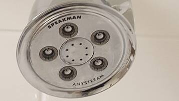 Un cabezal de ducha con la marca 'SPEAKMAN' y el modelo 'ANYSTREAM' montado sobre una pared de azulejos blancos.