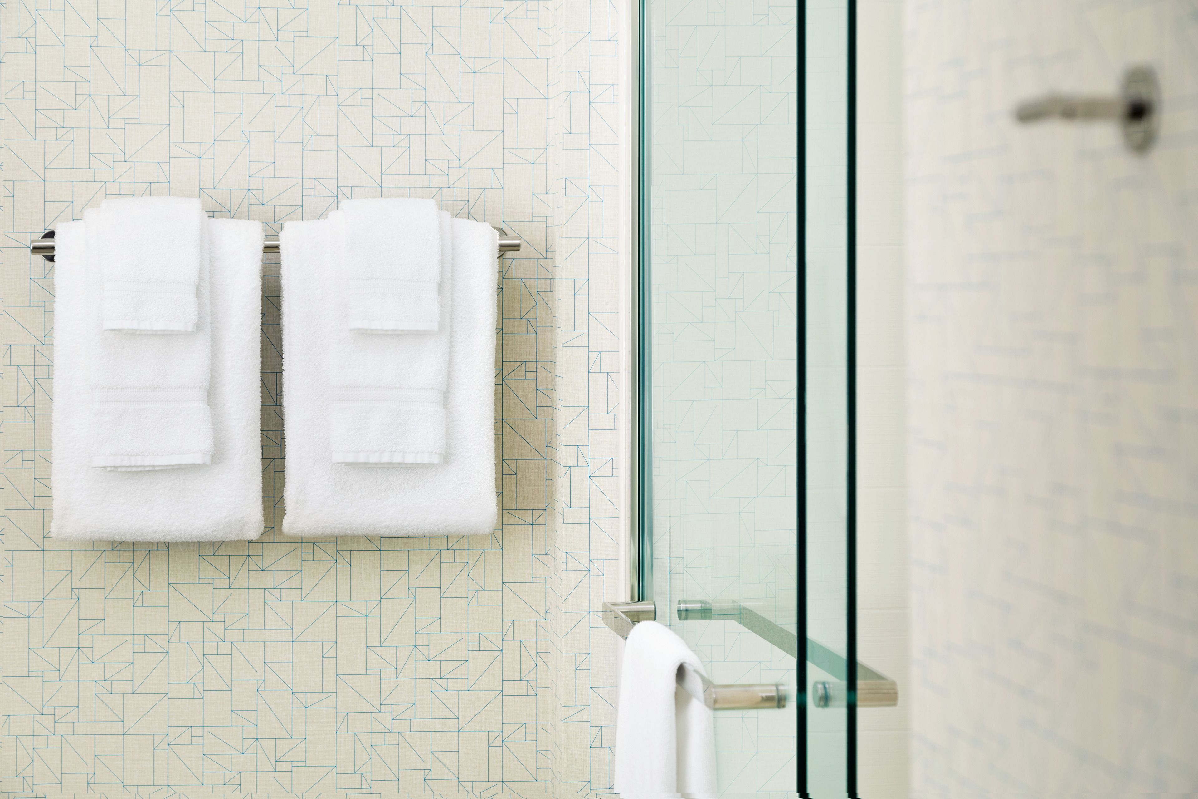 A bathroom with a geometric patterned wall, a glass shower enclosure, and two white towels hanging on a rack.