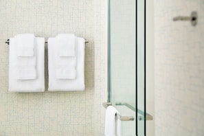 A bathroom with a geometric patterned wall, a glass shower enclosure, and two white towels hanging on a rack.