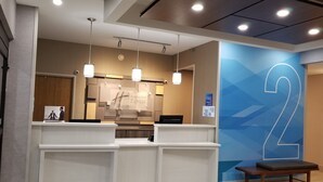 A hotel reception area with a large blue wall featuring a prominent number '2'. There are reception desks, a wooden bench, and overhead lighting. - Holiday Inn Express Indiana by IHG (Indiana)