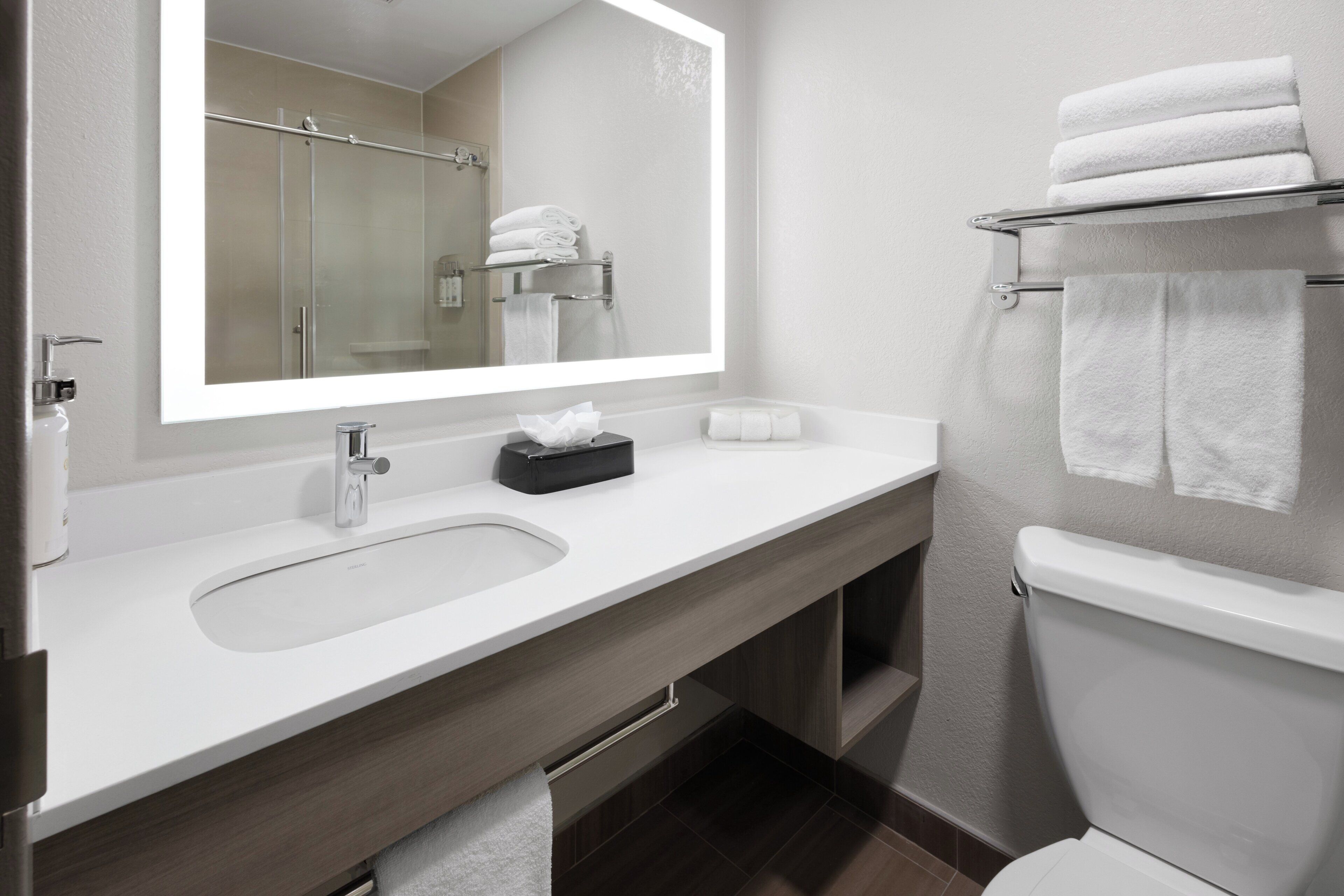 A modern bathroom with a large mirror, a sink, a toilet, and a towel rack.