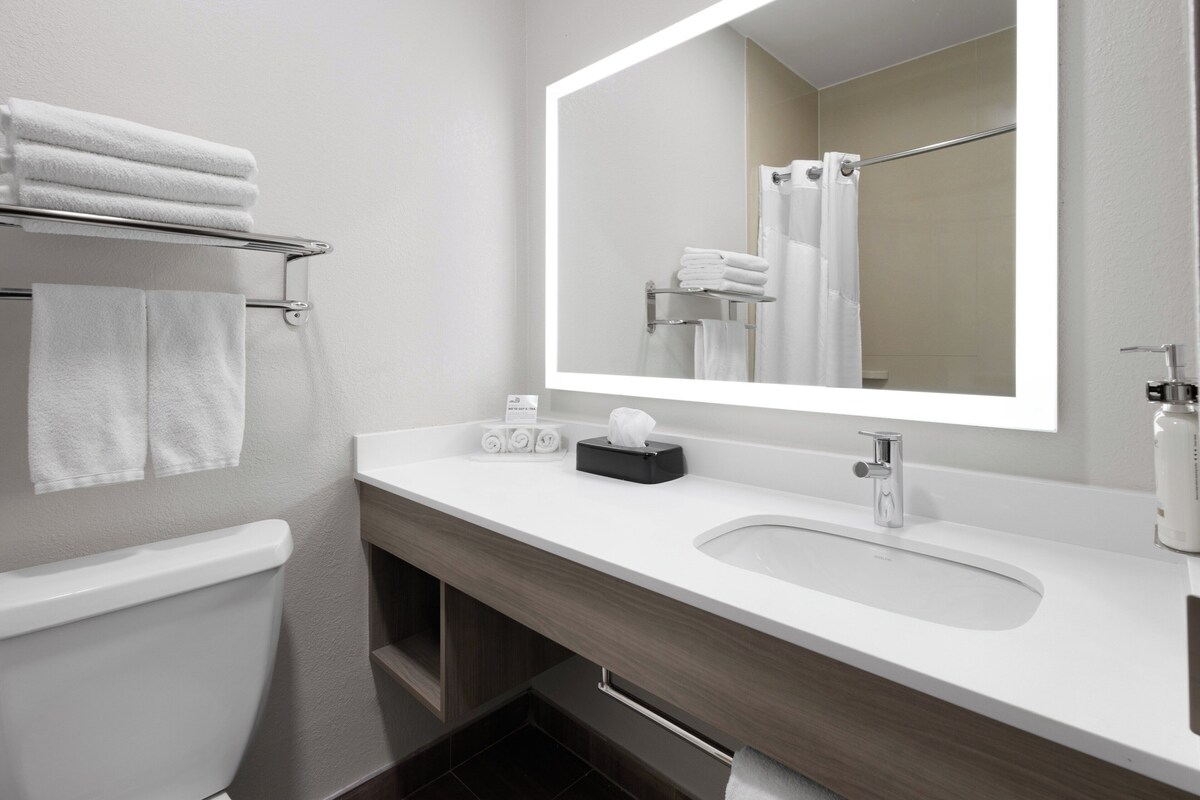 A modern bathroom with a white sink, a large mirror, and a towel rack with folded towels.