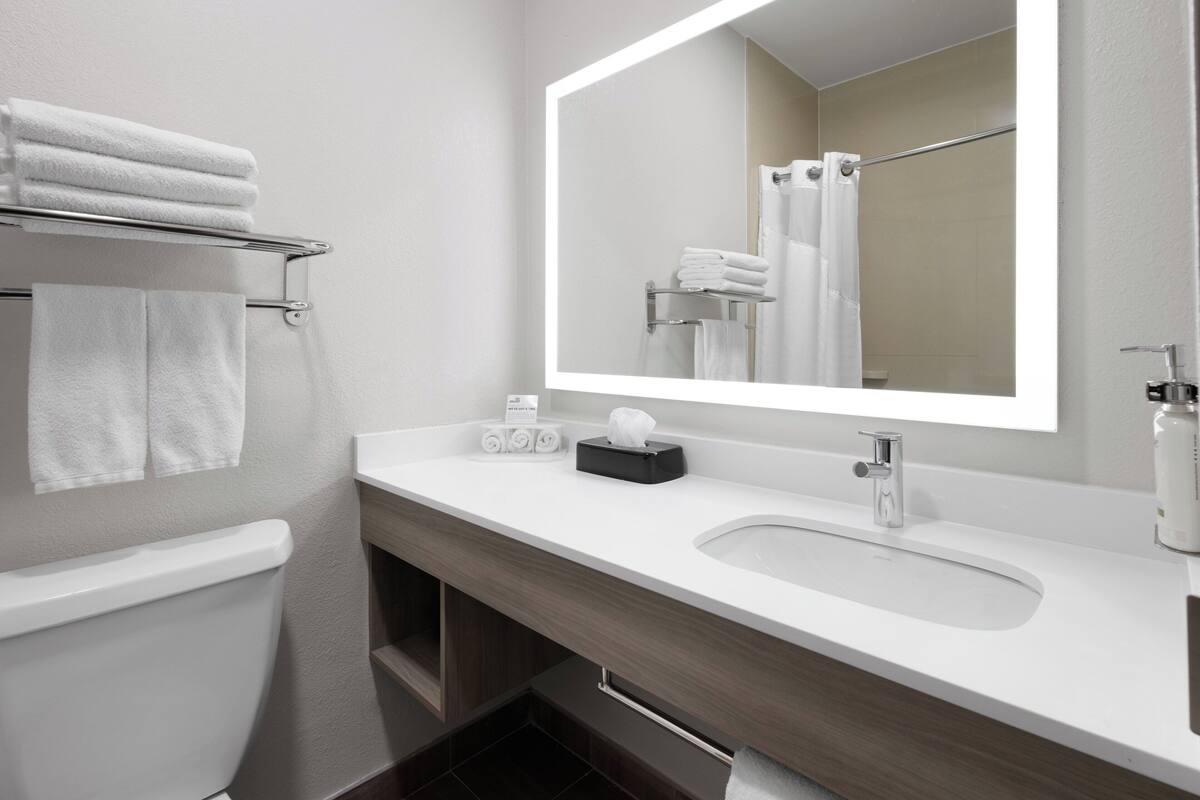 A modern bathroom with a white sink, a large mirror, and a towel rack with folded towels.
