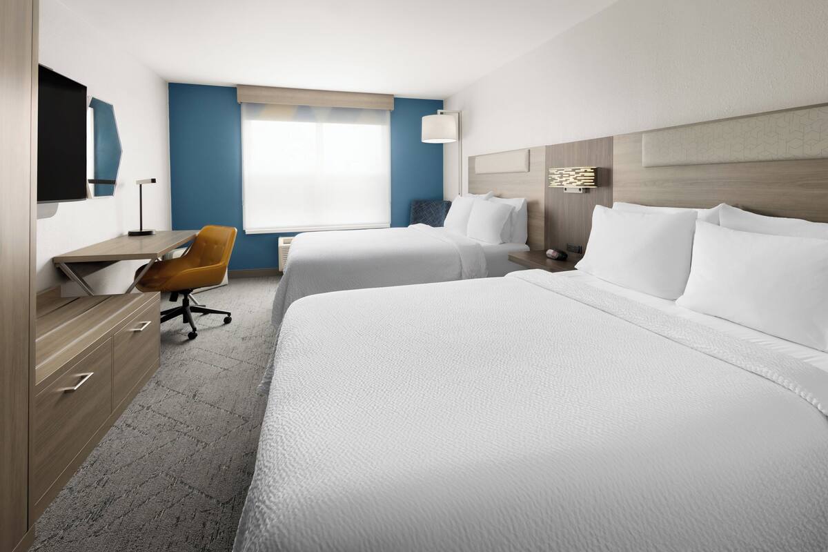A hotel room with two beds, a desk, a chair, and a large window.
