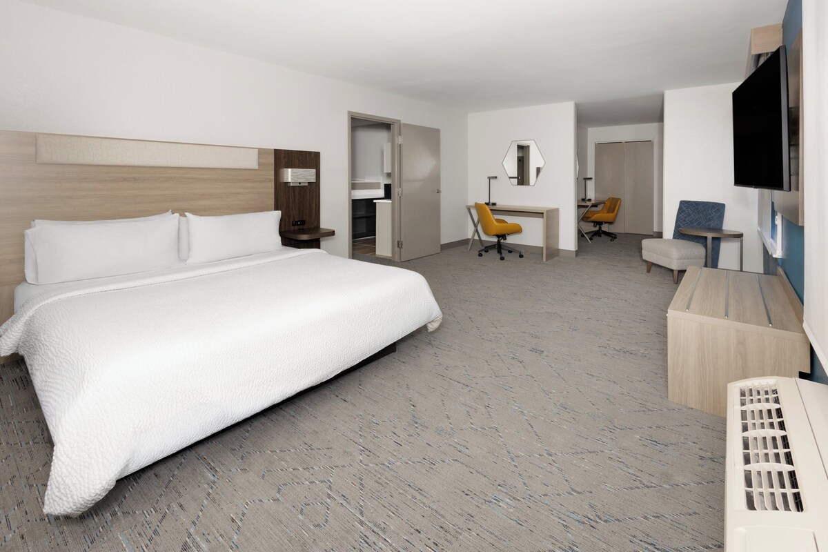 A hotel room with a large bed, a desk, a chair, a television, and a wardrobe.