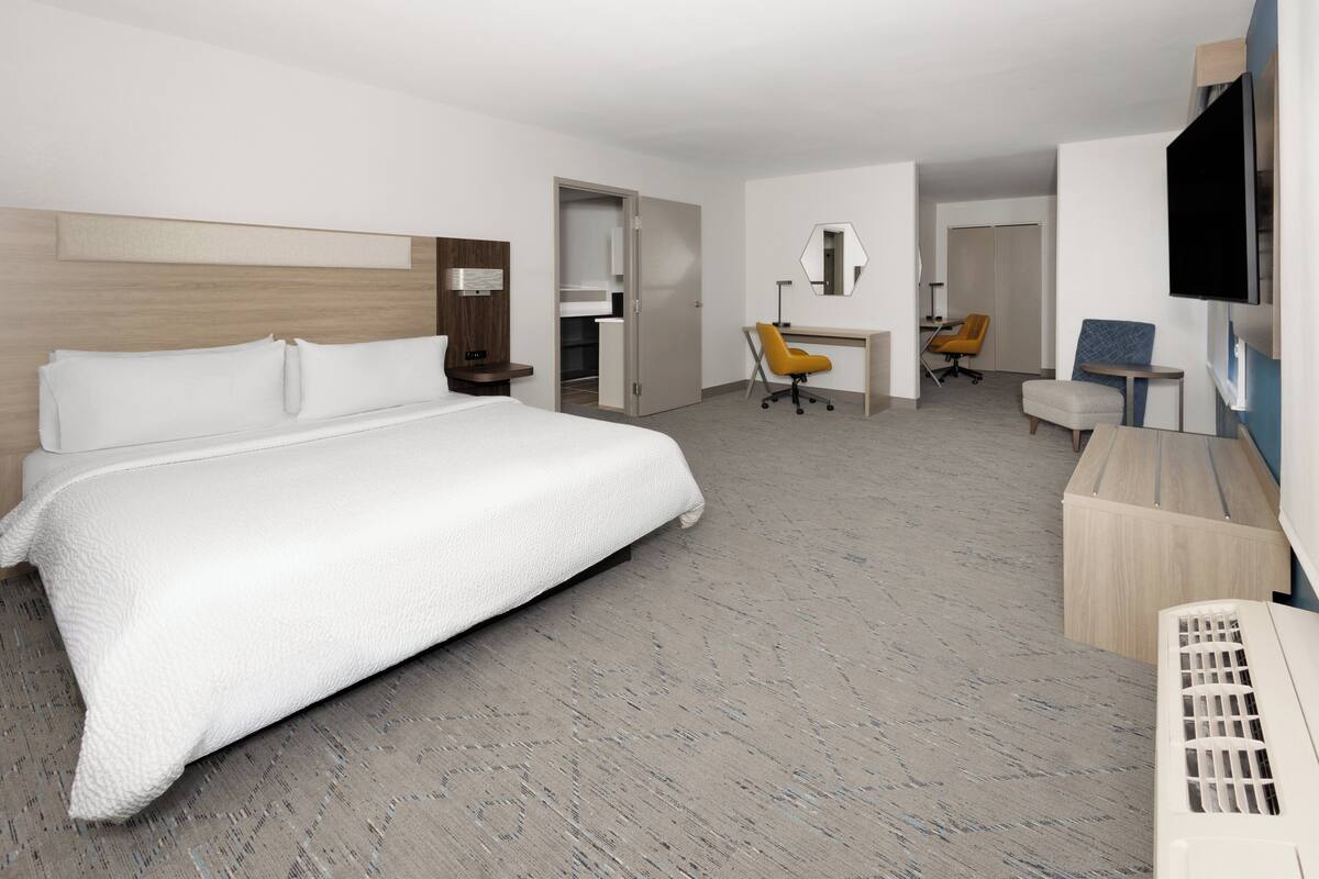 A hotel room with a large bed, a desk, a chair, a television, and a wardrobe.