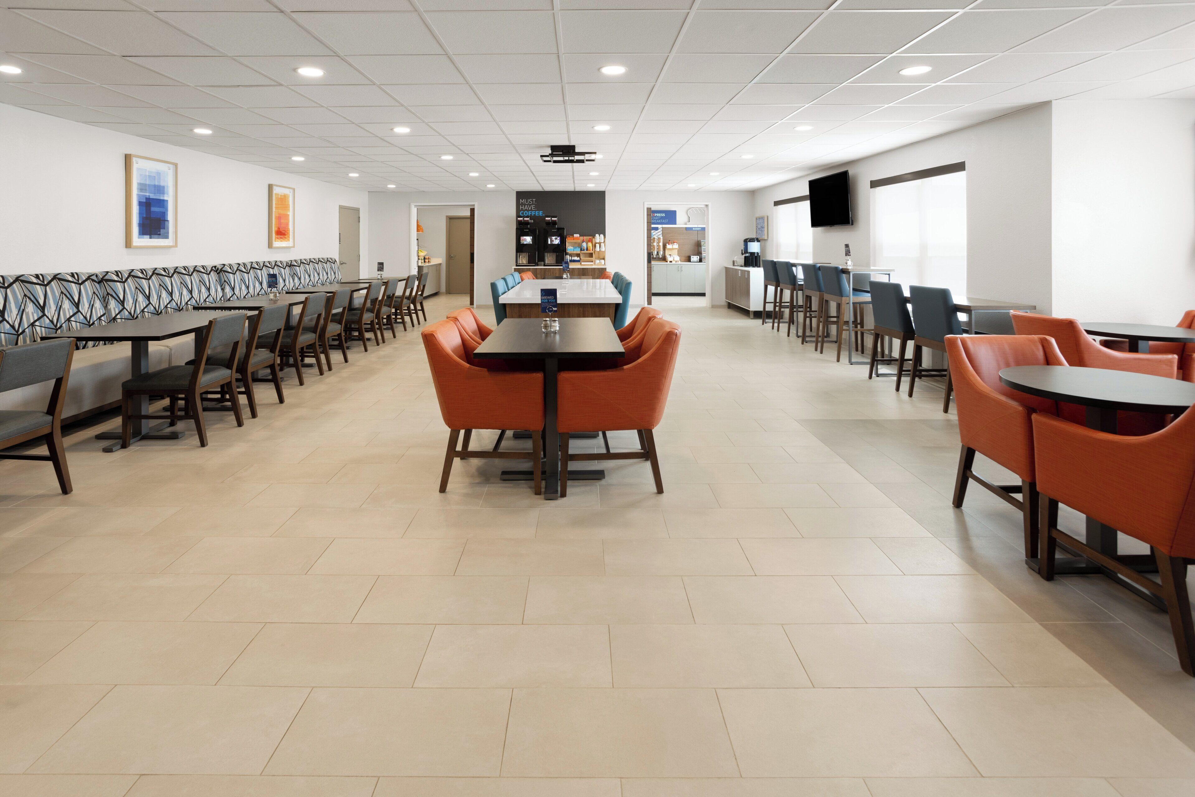 Un'ampia sala da pranzo con numerosi tavoli e sedie, un buffet centrale e un televisore a parete.