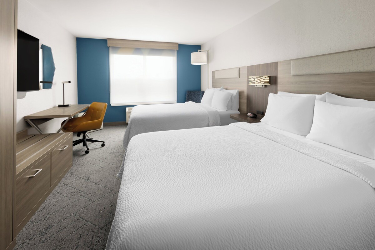 A hotel room with two beds, a desk, a chair, and a large window.