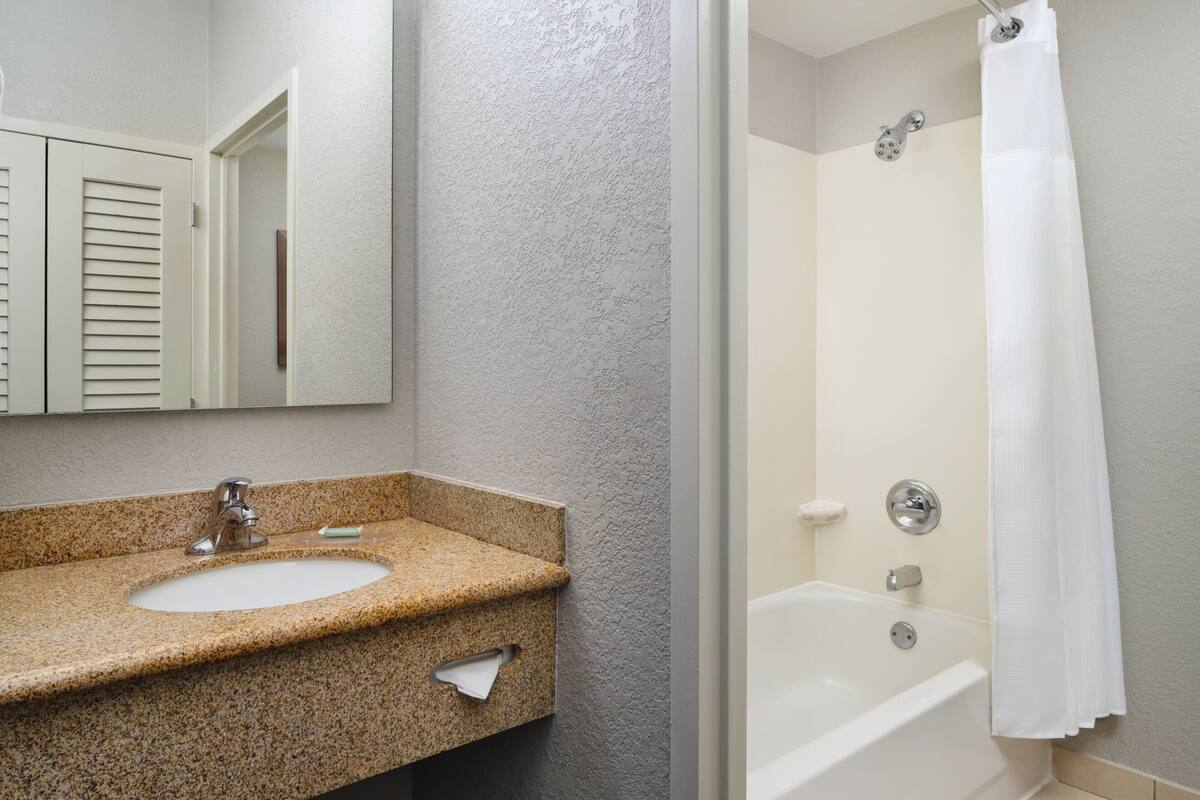 A bathroom with a granite countertop sink, a mirror, a shower with a white curtain, and a bathtub.