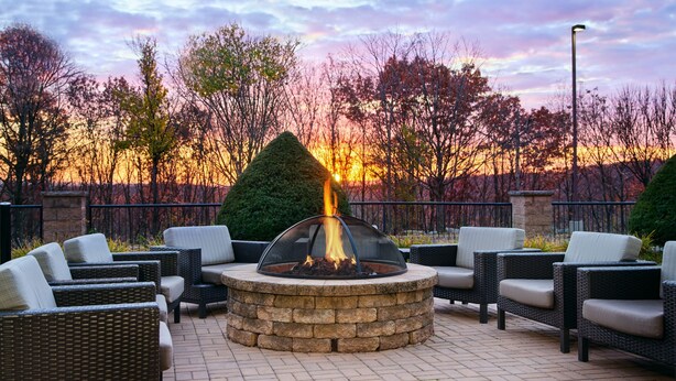 A circular outdoor seating area with a fire pit in the center, surrounded by wicker chairs and a stone wall. - Courtyard by Marriott Scranton Montage Mountain (Moosic)