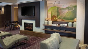 A modern living room with a flat-screen TV mounted above a fireplace, comfortable seating, and a decorative abstract painting. - Courtyard by Marriott Scranton Montage Mountain (Moosic)