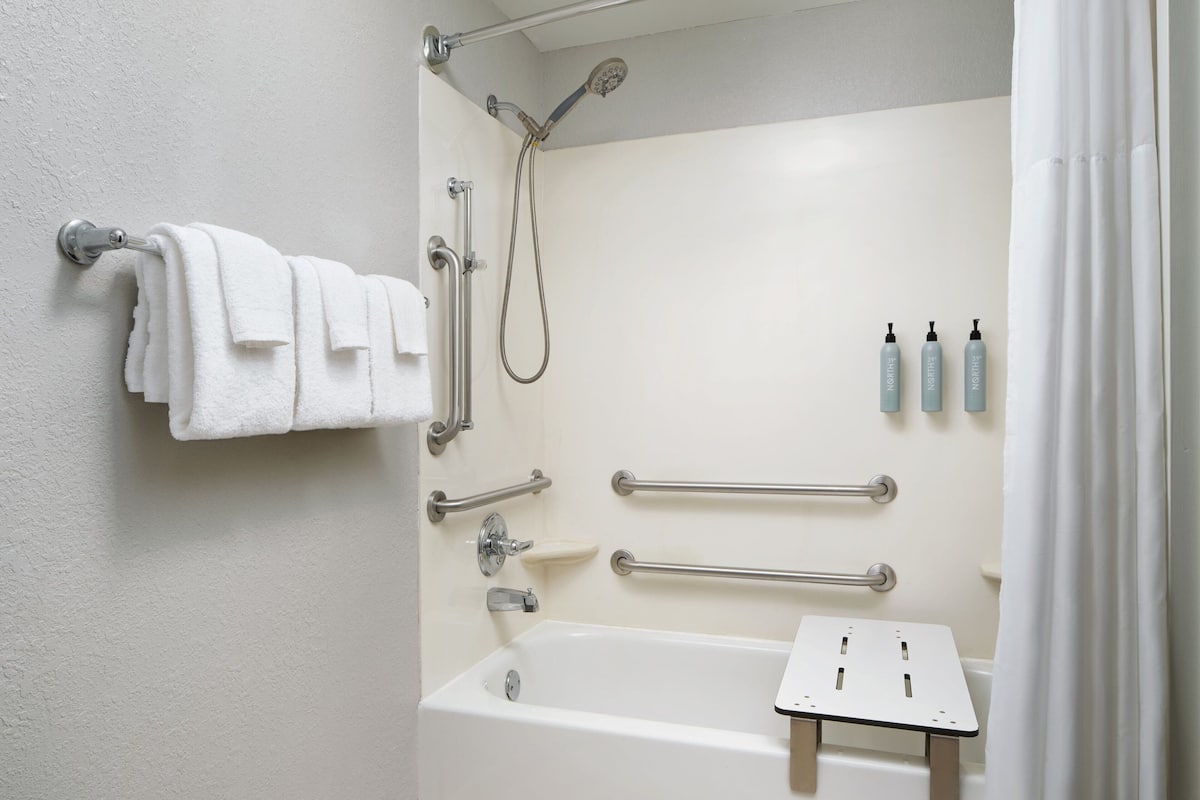 A bathroom with a bathtub, a shower, grab bars, and a towel rack.