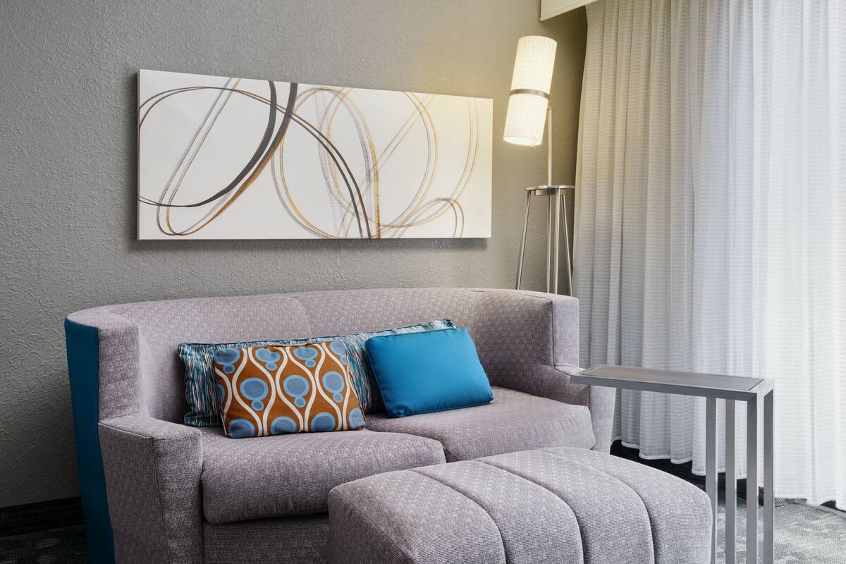 A modern living room with a grey sofa, a blue pillow, a floor lamp, and a large abstract painting on the wall.