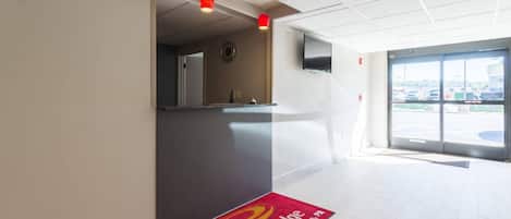 Zona de recepción de un hotel con un tapete de alfombra roja, un mostrador de recepción y un televisor montado en la pared.