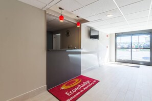 A hotel reception area with a red carpet mat, a reception desk, and a television mounted on the wall.