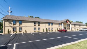 A motel with a parking lot, a red car parked in the lot, and a clear blue sky.